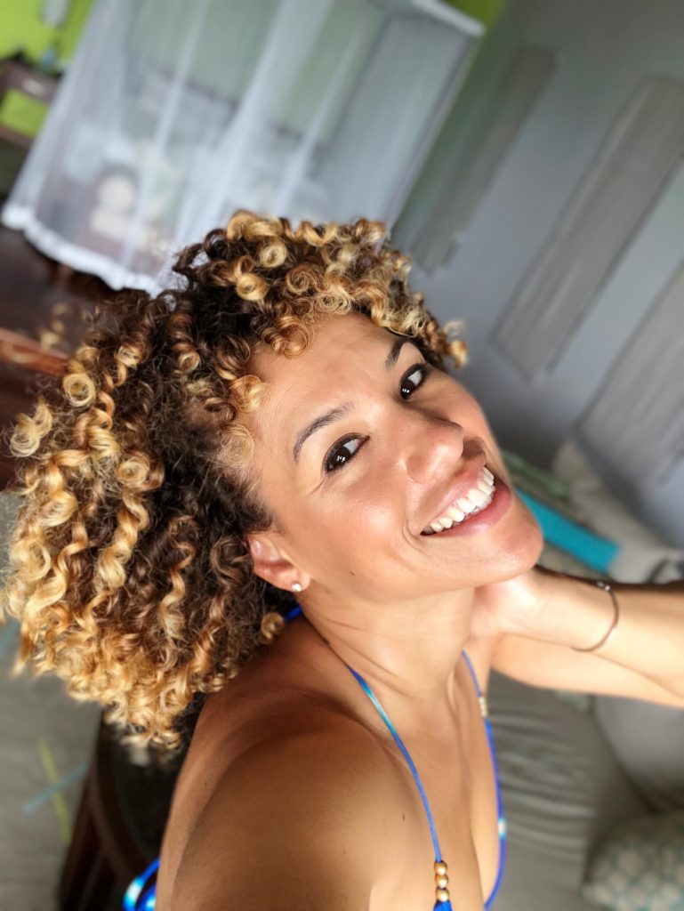 A selfie taken by a woman in Seychelles with short curly hair who is smiling with her head tilted back.