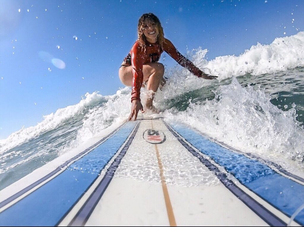 A woman crouched down and balancing on a blue and white striped surf board, riding a wave in Santa Teresa.