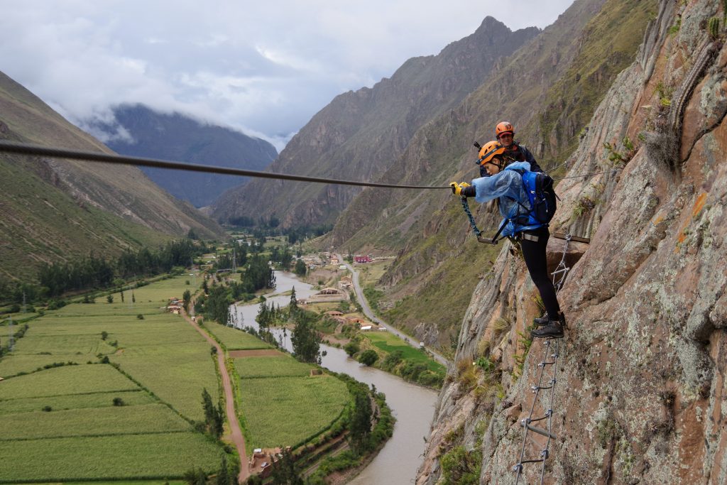 Woman carrying out her travel bucket list adventure and climbing a mountain going across a small and shaky cable bridge in Peru.